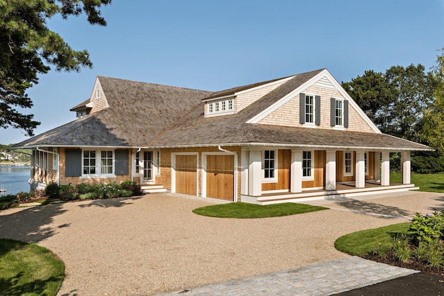 shingle-style home featuring an attached garage, a porch, gravel driveway, and a shingled roof