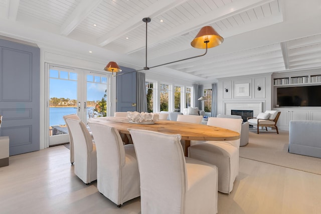 dining room featuring light wood-type flooring, a glass covered fireplace, french doors, and a water view