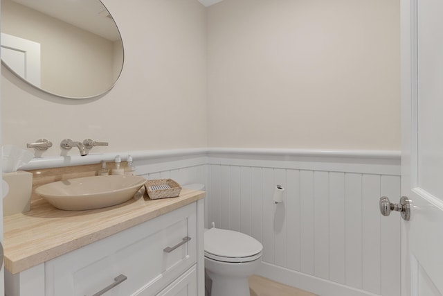 bathroom with a wainscoted wall, vanity, and toilet