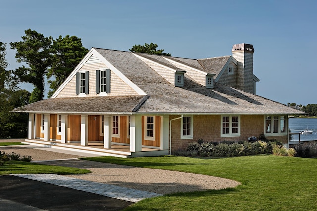 shingle-style home with a chimney, a porch, and a front yard