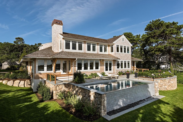 rear view of house with french doors, a yard, a chimney, a patio, and an outdoor pool