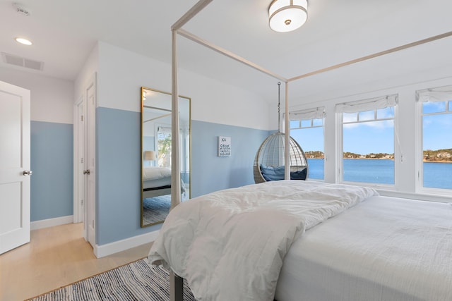 bedroom with a water view, light wood finished floors, multiple windows, and visible vents