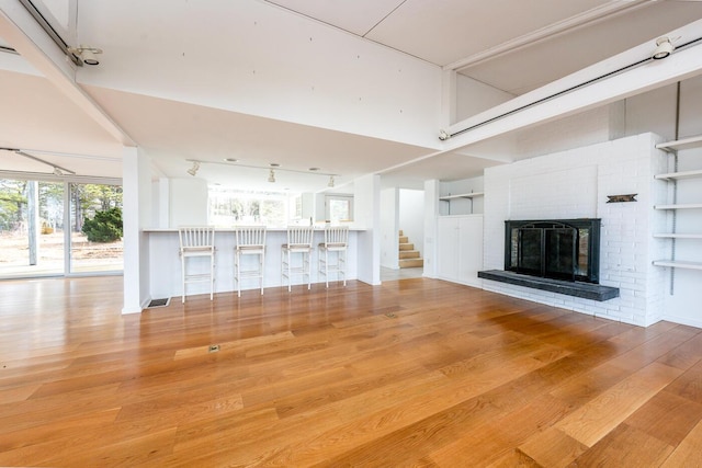 unfurnished living room featuring a brick fireplace, wood-type flooring, and a high ceiling