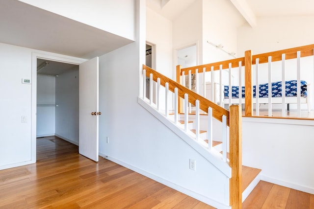 staircase featuring lofted ceiling with beams and wood-type flooring