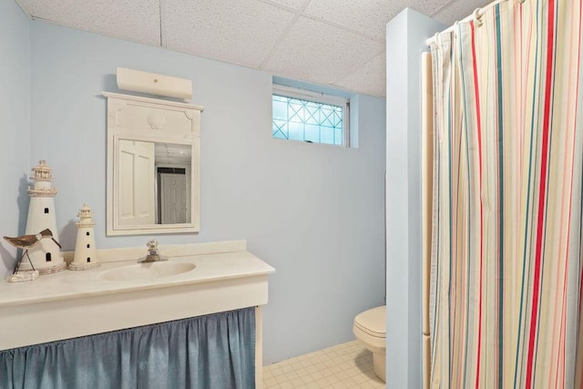 bathroom with a drop ceiling, vanity, toilet, and walk in shower