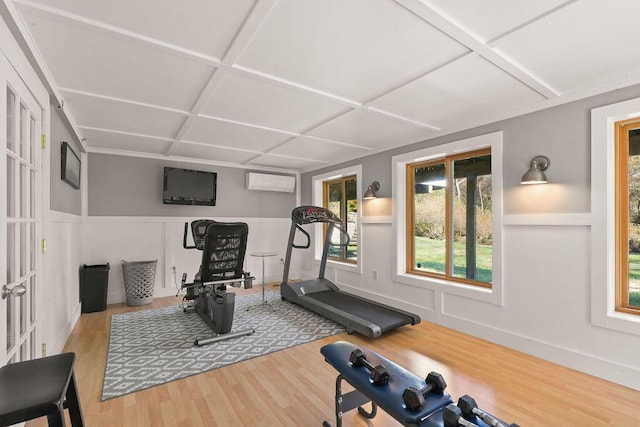 workout room featuring coffered ceiling, a wall mounted air conditioner, and light wood-type flooring