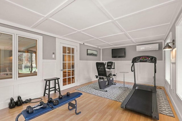 exercise room featuring wood-type flooring, coffered ceiling, and a wall unit AC