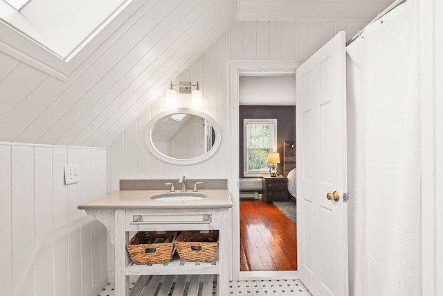 bathroom featuring vaulted ceiling, vanity, and wood walls