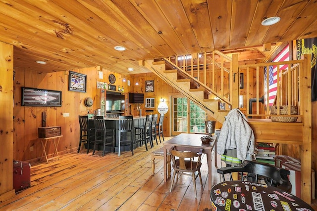 dining room with wood-type flooring, bar, wooden ceiling, and wood walls