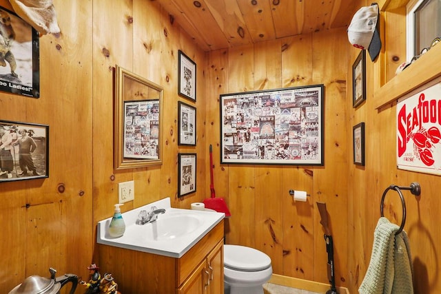 bathroom featuring vanity, wooden walls, wooden ceiling, and toilet