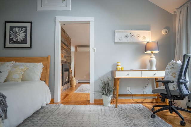 bedroom featuring a wall unit AC, a baseboard radiator, wood finished floors, lofted ceiling, and an office area