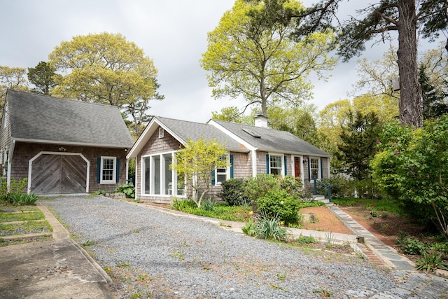 view of front of property featuring a shingled roof, a chimney, gravel driveway, an outbuilding, and a garage