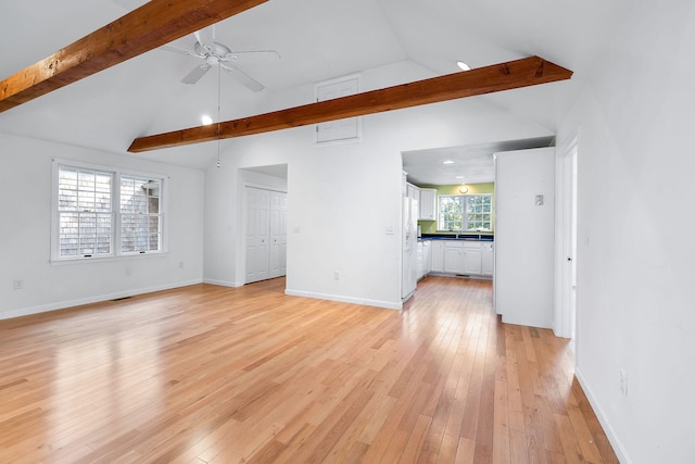 unfurnished living room with light hardwood / wood-style floors, lofted ceiling with beams, and plenty of natural light