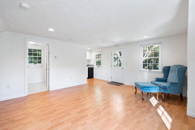living area with vaulted ceiling, a healthy amount of sunlight, and light hardwood / wood-style flooring