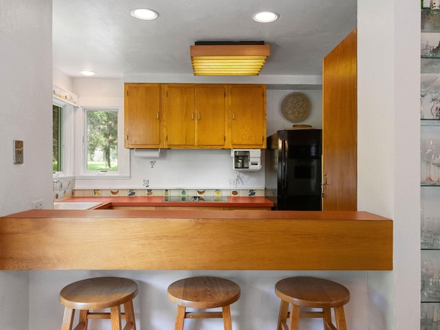 24 Sparrowhawk Rd, Orleans, MA 02653 - kitchen featuring black appliances, a breakfast bar area, brown cabinetry, and recessed lighting
