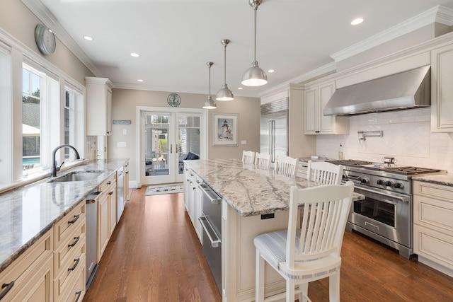 10 Shiverick Rd, East Dennis, MA 02641 - kitchen featuring wall chimney range hood, high end appliances, cream cabinetry, tasteful backsplash, and recessed lighting