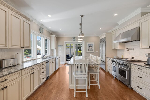 10 Shiverick Rd, East Dennis, MA 02641 - kitchen with premium appliances, cream cabinetry, wall chimney range hood, tasteful backsplash, and recessed lighting