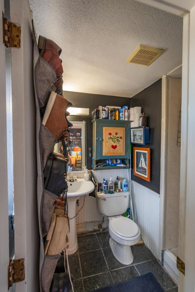 bathroom with a textured ceiling, toilet, and wood walls