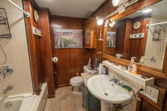 full bathroom featuring tiled shower / bath combo, tile patterned floors, sink, toilet, and wood walls