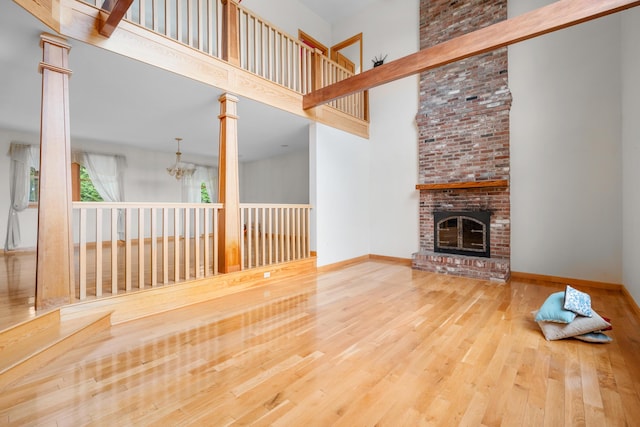 9 Priest Rd, Truro, MA 02666 - unfurnished living room featuring a high ceiling, wood finished floors, a brick fireplace, a chandelier, and ornate columns