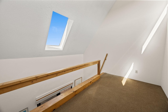 interior space featuring an upstairs landing, lofted ceiling with skylight, and carpet flooring