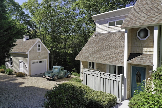 view of side of home featuring an outbuilding, driveway, and a shingled roof