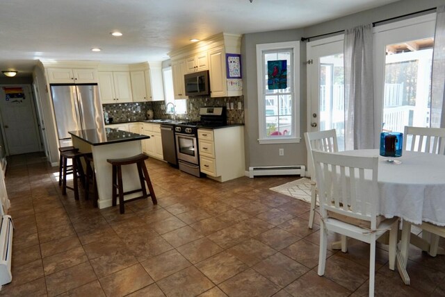 57 Camden Ln, Mashpee, MA 02649 - kitchen with stainless steel appliances, a baseboard heating unit, dark countertops, backsplash, and a kitchen bar