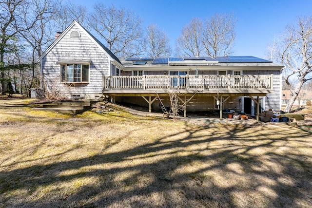 rear view of property with a lawn, a chimney, roof mounted solar panels, and a wooden deck