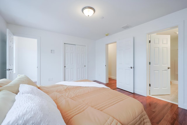 bedroom with a closet, visible vents, baseboards, and wood finished floors