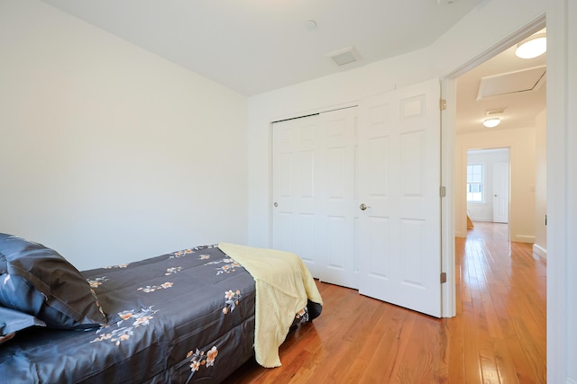 bedroom featuring a closet, visible vents, light wood-style floors, attic access, and baseboards