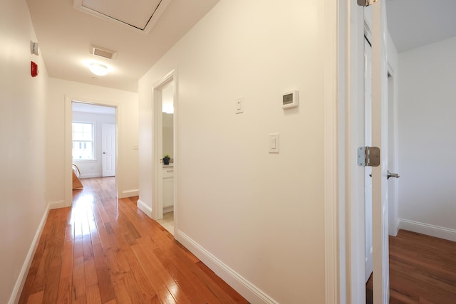 hall featuring baseboards, visible vents, and light wood finished floors