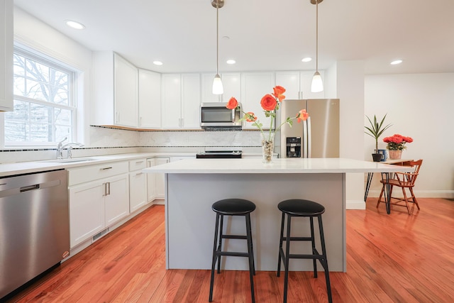 kitchen with light wood finished floors, appliances with stainless steel finishes, a breakfast bar, a center island, and light countertops