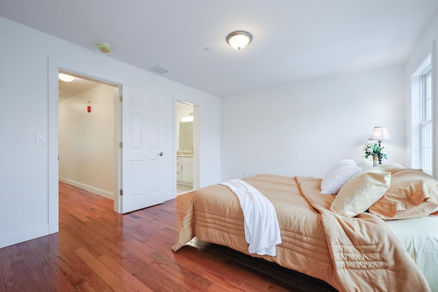 bedroom with connected bathroom, baseboards, and wood finished floors