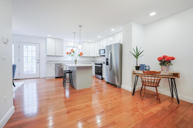 kitchen with light wood finished floors, a kitchen breakfast bar, a center island, stainless steel appliances, and light countertops