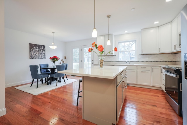 kitchen with light wood-style flooring, electric range, light countertops, tasteful backsplash, and a kitchen bar