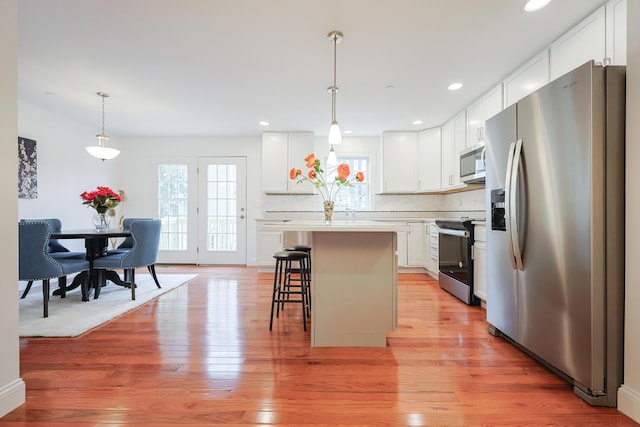 kitchen with appliances with stainless steel finishes, light wood-type flooring, a kitchen bar, and a healthy amount of sunlight