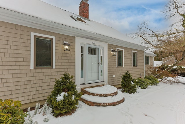 snow covered property entrance with a chimney