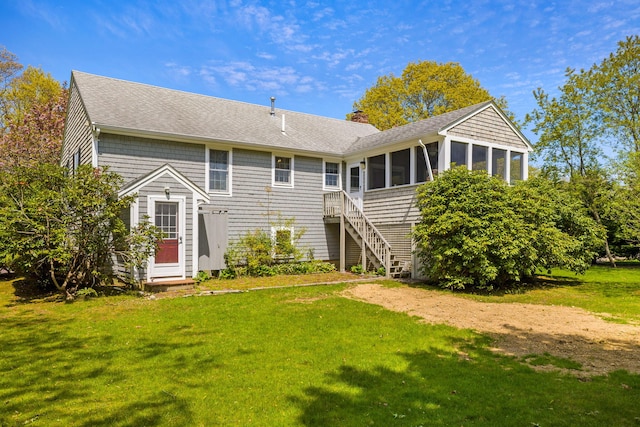 rear view of house with a sunroom, roof with shingles, and a lawn