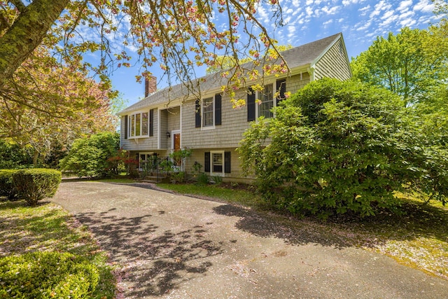 bi-level home with a chimney, driveway, and roof with shingles
