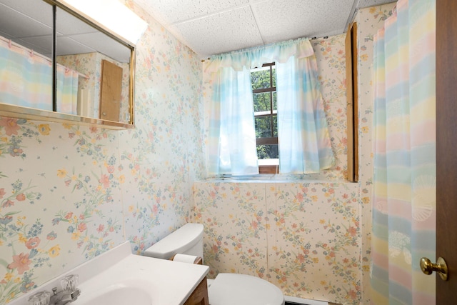 bathroom with a drop ceiling, toilet, vanity, and wallpapered walls