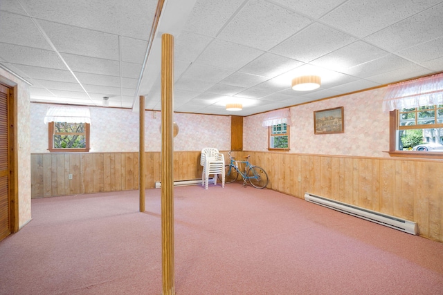 below grade area featuring baseboard heating, wallpapered walls, wooden walls, a drop ceiling, and plenty of natural light