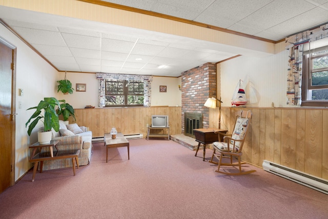 sitting room with wood walls, baseboard heating, a drop ceiling, carpet, and a brick fireplace