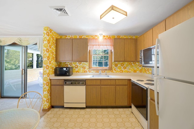 kitchen with white appliances, a sink, light countertops, brown cabinetry, and wallpapered walls