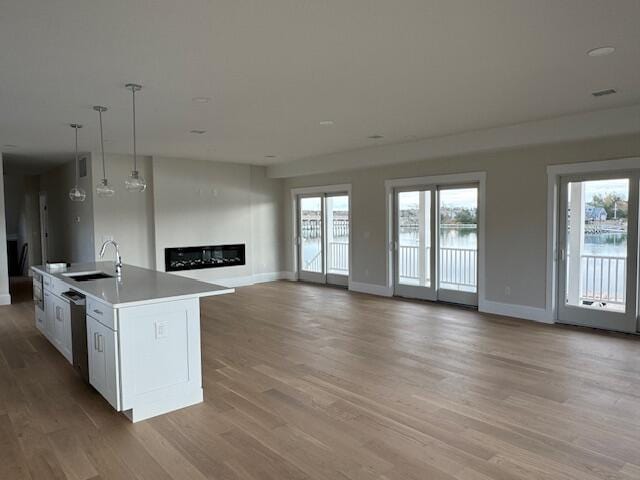 kitchen with white cabinetry, stainless steel dishwasher, sink, decorative light fixtures, and a center island with sink