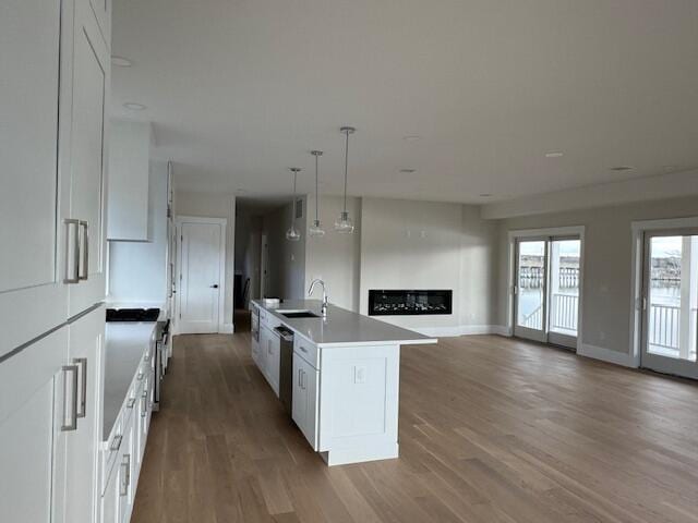 kitchen featuring white cabinets, hanging light fixtures, a kitchen island with sink, and sink