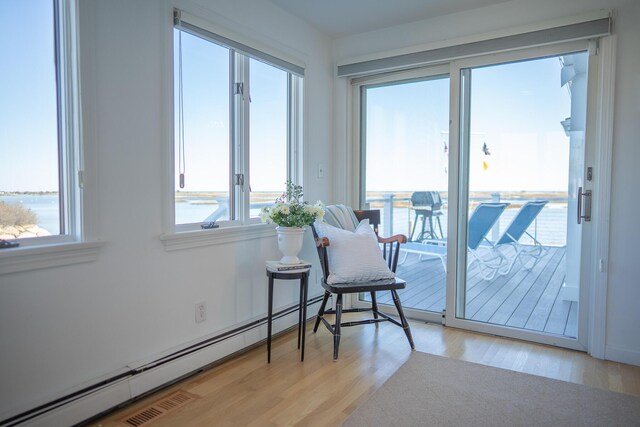 sitting room featuring a water view, baseboard heating, and light wood-type flooring