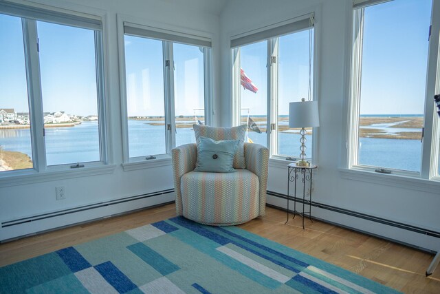 sunroom featuring a water view, baseboard heating, and wood finished floors