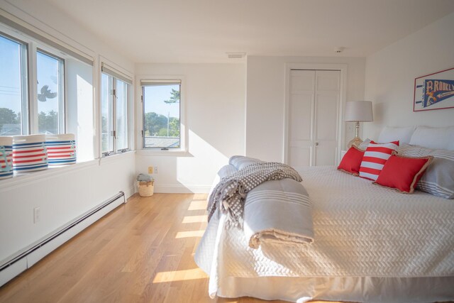 bedroom with a closet, visible vents, wood finished floors, and a baseboard radiator