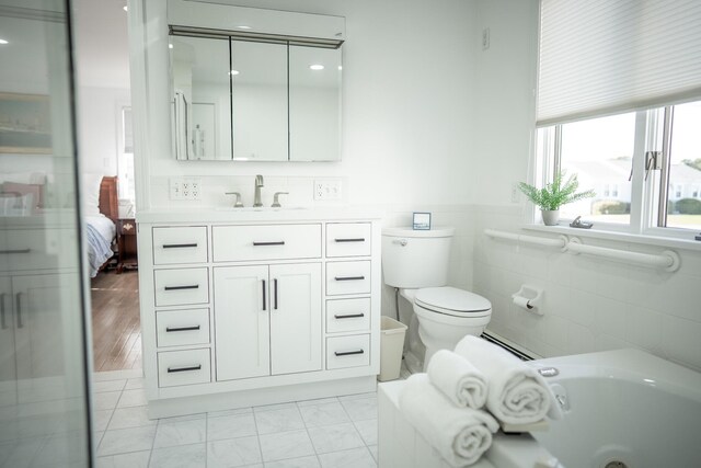 full bath with wainscoting, a bathing tub, a baseboard radiator, vanity, and toilet