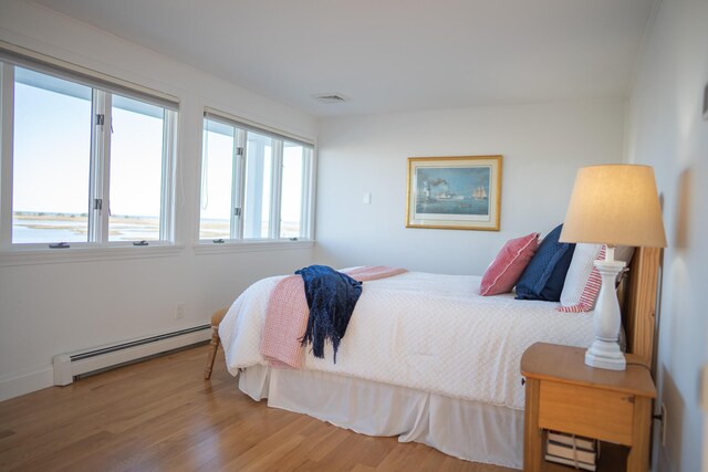bedroom with wood finished floors, a baseboard heating unit, visible vents, and multiple windows